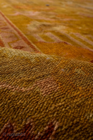 This antique Oushak rug glows with rich, warm tones of golden saffron, soft apricot, and muted blush. Its geometric medallion-and-corner design is framed by a beautifully drawn border, giving the rug a  ...