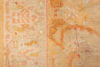 This antique Oushak rug features a warm, time-softened palette of gold, apricot, and blush tones, anchored by a central medallion design with playful floral and vine motifs. The wide border with decorative  ...