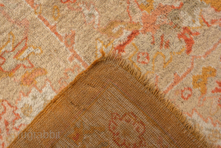 This antique Oushak rug features a warm, time-softened palette of gold, apricot, and blush tones, anchored by a central medallion design with playful floral and vine motifs. The wide border with decorative  ...