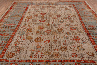 This antique Oushak rug, woven circa 1900, features a captivating Tree of Life design with stylized floral and botanical motifs cascading across an ivory field. The delicate, painterly pattern is framed by  ...