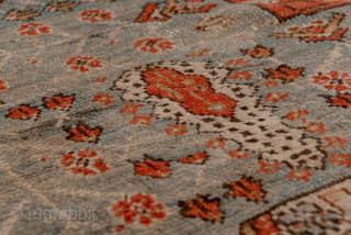This antique Oushak rug, woven circa 1900, features a captivating Tree of Life design with stylized floral and botanical motifs cascading across an ivory field. The delicate, painterly pattern is framed by  ...