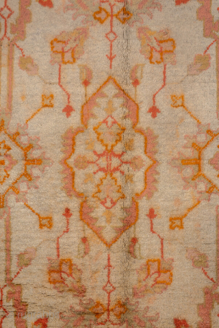 This antique Oushak rug, woven circa 1920, boasts a luminous palette of soft coral, apricot, and golden hues accented by subtle ivory highlights. Its allover pattern features stylized floral and geometric motifs  ...
