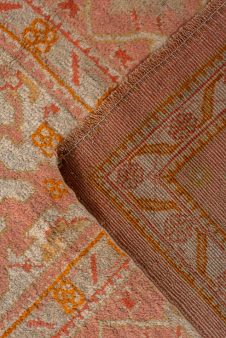 This antique Oushak rug, woven circa 1920, boasts a luminous palette of soft coral, apricot, and golden hues accented by subtle ivory highlights. Its allover pattern features stylized floral and geometric motifs  ...