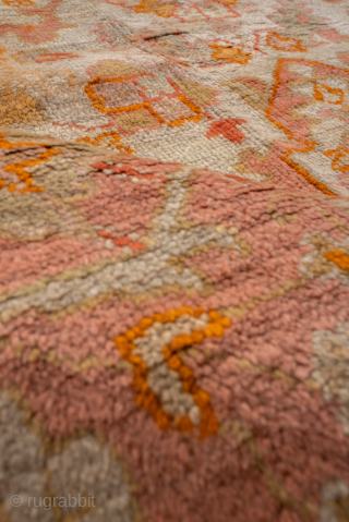 This antique Oushak rug, woven circa 1920, boasts a luminous palette of soft coral, apricot, and golden hues accented by subtle ivory highlights. Its allover pattern features stylized floral and geometric motifs  ...