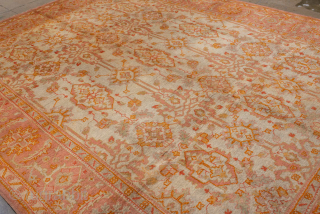 This antique Oushak rug, woven circa 1920, boasts a luminous palette of soft coral, apricot, and golden hues accented by subtle ivory highlights. Its allover pattern features stylized floral and geometric motifs  ...