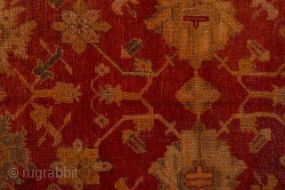 This antique Turkish Oushak rug, woven circa 1900, features a striking deep red field adorned with soft gold and muted blue floral motifs. The wide, decorative border frames the design beautifully, showcasing  ...
