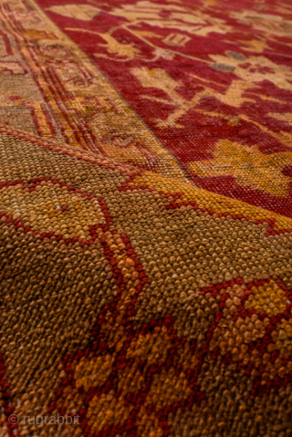 This antique Turkish Oushak rug, woven circa 1900, features a striking deep red field adorned with soft gold and muted blue floral motifs. The wide, decorative border frames the design beautifully, showcasing  ...