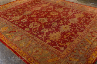 This antique Turkish Oushak rug, woven circa 1900, features a striking deep red field adorned with soft gold and muted blue floral motifs. The wide, decorative border frames the design beautifully, showcasing  ...