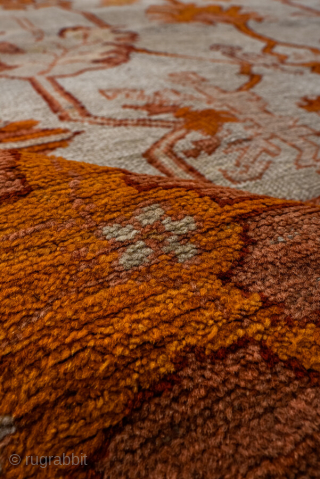 This antique Oushak rug, woven circa 1900 in Western Anatolia, showcases the region’s signature large-scale, open design with striking color contrasts. The ivory ground is adorned with an allover floral lattice rendered  ...