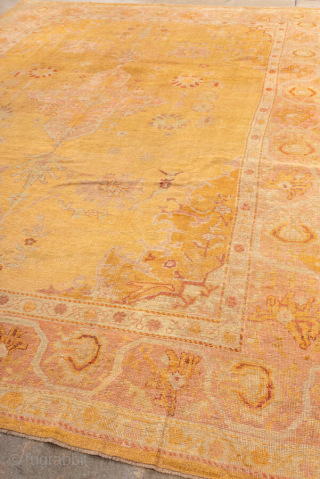 This antique Oushak rug features a luminous golden ground with soft rose undertones, creating a warm and inviting palette that is both refined and versatile. At the center, a faintly drawn medallion  ...