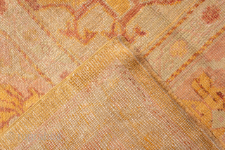 This antique Oushak rug features a luminous golden ground with soft rose undertones, creating a warm and inviting palette that is both refined and versatile. At the center, a faintly drawn medallion  ...