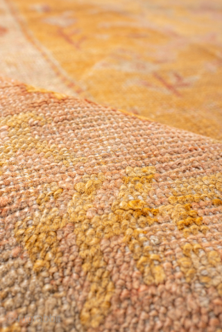 This antique Oushak rug features a luminous golden ground with soft rose undertones, creating a warm and inviting palette that is both refined and versatile. At the center, a faintly drawn medallion  ...