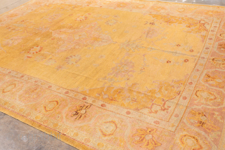 This antique Oushak rug features a luminous golden ground with soft rose undertones, creating a warm and inviting palette that is both refined and versatile. At the center, a faintly drawn medallion  ...