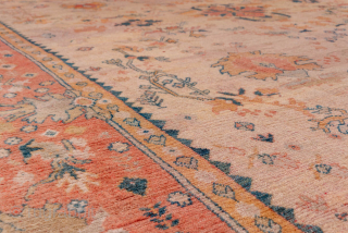 This magnificent large-scale antique Oushak rug features a serene and graceful composition typical of early 20th-century Western Turkish weaving. The soft coral field hosts a loosely drawn floral medallion pattern rendered in  ...