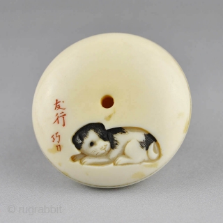 Japanese ivory manju netsuke carved in low relief  with a boy and puppy, 
the reverse is carved with another puppy end the carver's signature.
The details stained in black and red ink.
  ...