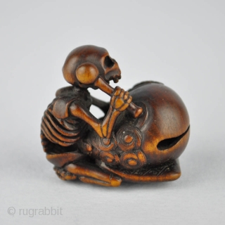 Japanese wood netsuke finely carved with the skeleton of the priest Danka beating the mokugyo, 
the wooden bell used in the Buddhist liturgy. The himotoshi ringed in horn. Signed: Juzan 寿山
19th century.  ...