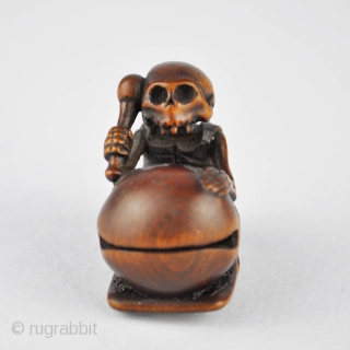 Japanese wood netsuke finely carved with the skeleton of the priest Danka beating the mokugyo, 
the wooden bell used in the Buddhist liturgy. The himotoshi ringed in horn. Signed: Juzan 寿山
19th century.  ...