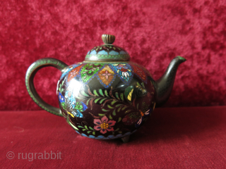 Antique Meiji era Japanese Cloisonne footed teapot. The teapot’s body is decorated all over with scrolling foliage and multicolored butterflies, flowers on a black background while the spout and the base are  ...