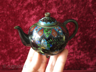 Antique Meiji era Japanese Cloisonne footed teapot. The teapot’s body is decorated all over with scrolling foliage and multicolored butterflies, flowers on a black background while the spout and the base are  ...