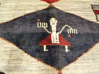 A very thick gabbeh, woven mainly with undyed soft wool. The central large figure has some triangular hankerchieves, so she might be dancing one of the traditional Qashqai dances. Her hands are  ...