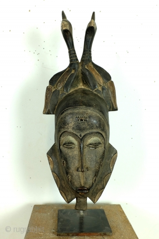 Baoulé, 
The BAOULE masks are known in African art for the smoothness of their features, protruding mouth, half closed eyes. 
The mask is topped with a headdress decorated with towering braids. 
The  ...