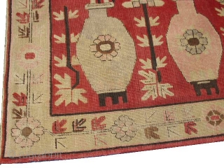 This circa 1920 Khotan #6203 
antique carpet measures 4’11” x 8’1”. It has four standing urns in pink and green on a red ground with flowers sprouting from each. It has a  ...