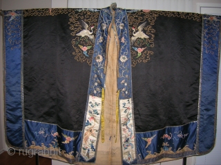 PRIEST ROBE. 
 
19th Century
The dark blue ground is elaborately worked on the front and back in satin stitch and couched gold threads showing dragons, cranes, bats, precious objects and auspicious symbols
Center  ...