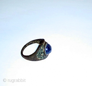 A SAPPHIRE INSET BRONZE RING PROBABLY SAMANID/ SELJUK 12TH CENTURY

The conical bezel set with a lightly faceted cabochon blue sapphire, the shank of lozenge section narrowing at each end    