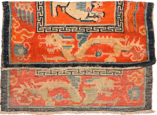Tibetan over-saddle carpet (masho) featuring two playful-looking snow lions chasing a central flaming jewel in an orange center field. The outer border consist of dragons and phoenixes on somewhat more redish background  ...