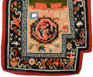 Tibetan under-saddle carpet or makden.  A single frolicking dragon is enclosed inside a mandala shaped outline on either side with flowers lightly scattered in the main field. The main outer border  ...