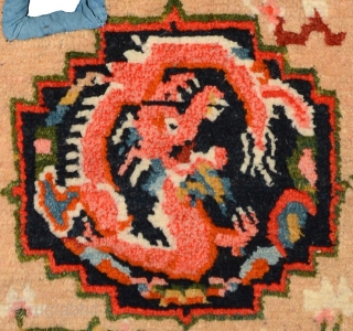 Tibetan under-saddle carpet or makden.  A single frolicking dragon is enclosed inside a mandala shaped outline on either side with flowers lightly scattered in the main field. The main outer border  ...