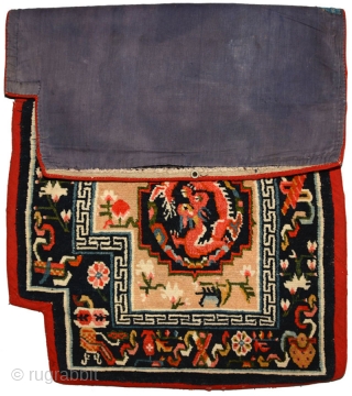Tibetan under-saddle carpet or makden.  A single frolicking dragon is enclosed inside a mandala shaped outline on either side with flowers lightly scattered in the main field. The main outer border  ...
