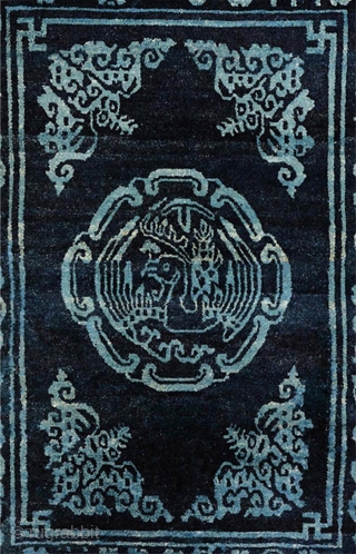 Two-toned naturally dyed Tibetan seating carpet – or shugden - with light blue coloured motifs of various sorts over a darker blue background. The outer border consist of assorted esoteric symbols while  ...