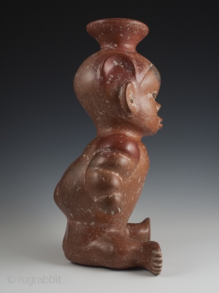 Seated dwarf vessel, Colima, West Mexico. Earthenware, slip, 11" (28 cm) high. 100 BC - 250 AD.

A reddish-brown painted earthenware seated dwarf with out-turned legs and bulging muscular arms. He wears a  ...