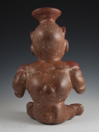 Seated dwarf vessel, Colima, West Mexico. Earthenware, slip, 11" (28 cm) high. 100 BC - 250 AD.

A reddish-brown painted earthenware seated dwarf with out-turned legs and bulging muscular arms. He wears a  ...