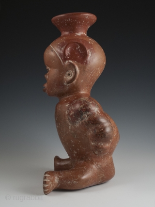 Seated dwarf vessel, Colima, West Mexico. Earthenware, slip, 11" (28 cm) high. 100 BC - 250 AD.

A reddish-brown painted earthenware seated dwarf with out-turned legs and bulging muscular arms. He wears a  ...