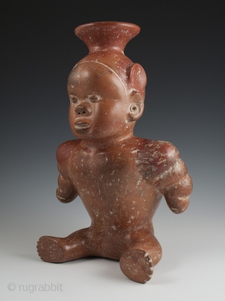 Seated dwarf vessel, Colima, West Mexico. Earthenware, slip, 11" (28 cm) high. 100 BC - 250 AD.

A reddish-brown painted earthenware seated dwarf with out-turned legs and bulging muscular arms. He wears a  ...