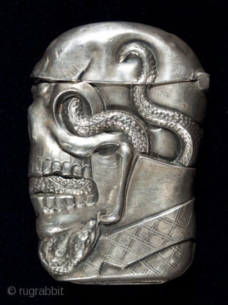 Match safe,
Unknown manufacturer.
Sterling silver.
2.5" (6.3 cm) high.
c. 1895.
This rare match safe is marked STERLING and there is a pinched striker on the bottom. A serpent winds through a dapper skull's sye sockets,  ...