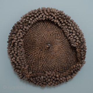 Chief's hat,
Pende tribe, D.R. Congo.
Fiber, mud, coins, beads, string.
6.5" (16.5 cm) diameter.
Early 20th century.

These 'seeds' are made of small bundles of fiber dipped in mud and affixed to a spiral stitched string  ...